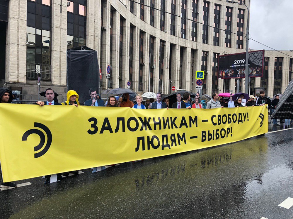 «Открытая Россия» развернула  на митинге  баннер «Заложникам — свободу! Людям — выбор!». За баннером размещены картонные фигуры независимых кандидатов, которые находятся под арестом